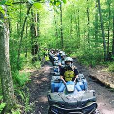 A row of ATV riders on a forest trail.