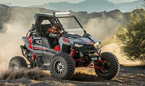 A gray and red RZR races through a desert setting.